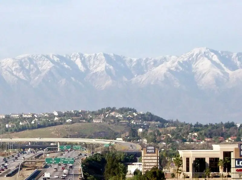 The Interstate 15 and State Route 91 interchange in Corona, California, with snow-capped mountains behind the city